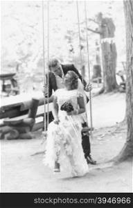 Black and white photo of happy kissing newlyweds on swing at forest
