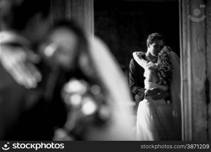 Black and white photo of hugging just married couple reflection in window