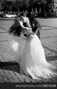 Black and white photo of kissing bride and groom on street at windy day