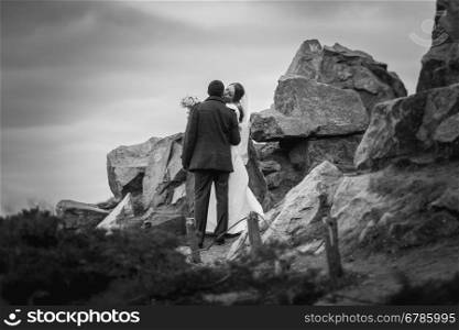 Black and white photo of kissing bride and groom on top of high mountain