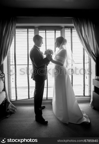 Black and white photo of newlyweds posing against big window