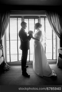 Black and white photo of newlyweds posing against big window