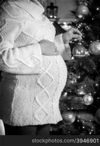 Black and white photo of pregnant woman posing at Christmas tree