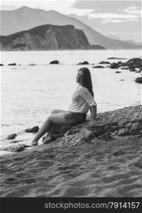 Black and white photo of sexy woman sitting on rock at deserted beach