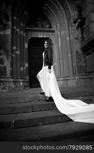 Black and white photo of sexy woman with long white veil walking on stairs of old abbey