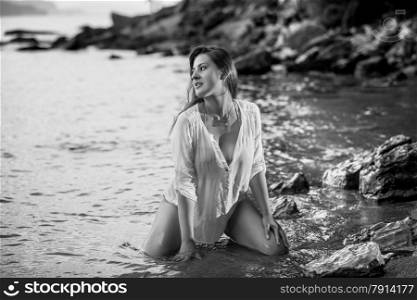 Black and white photo of sexy young woman kneeling at sea shore