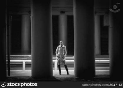 Black and white photo of sexy young woman posing between high columns under bridge