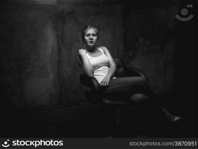 Black and white photo of sexy young woman sitting in chair at dark room