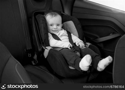 Black and white photo of smiling baby sitting in car seat