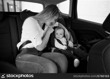 Black and white photo of smiling mother sitting on car backseat with her baby