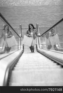 Black and white photo of smiling shopping woman on escalator