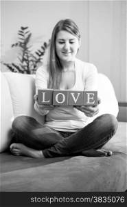 Black and white photo of smiling woman sitting on couch and holding word