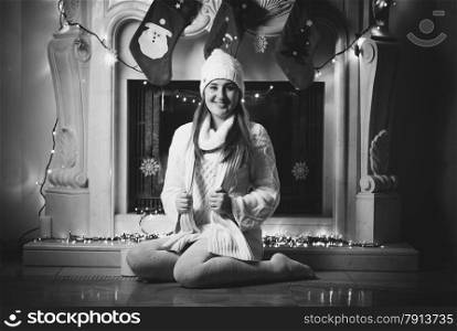 Black and white photo of smiling woman sitting on floor next to fireplace