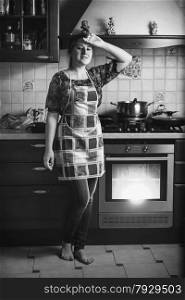 Black and white photo of tired housewife standing on kitchen