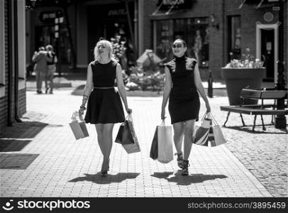 Black and white photo of two elegant women walking on street with shopping bags