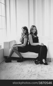 Black and white photo of two sexy woman sitting back to back on couch