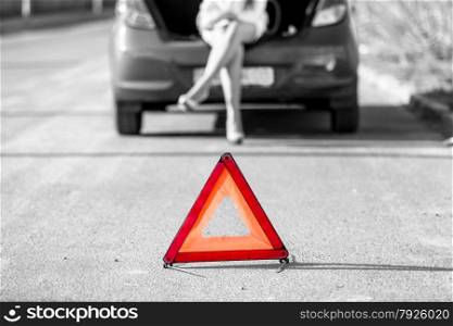 Black and white photo of woman sitting on broken car near red warning sign