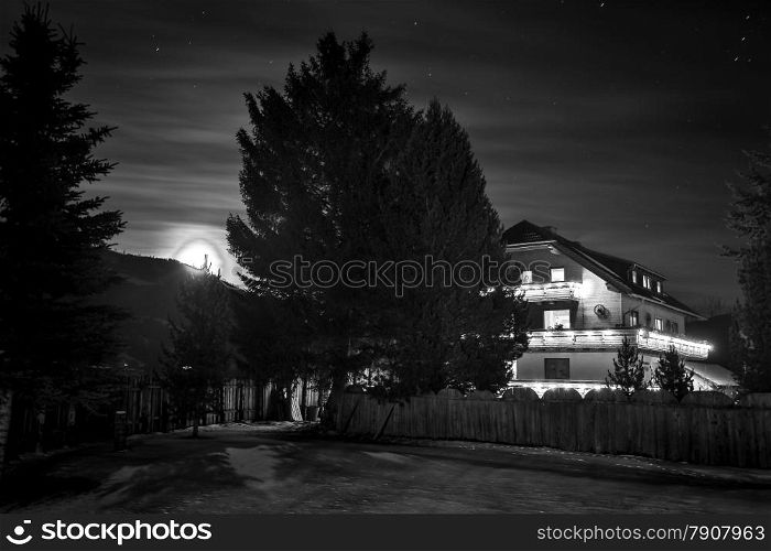 Black and white photo of wooden chalet in wood at starry night