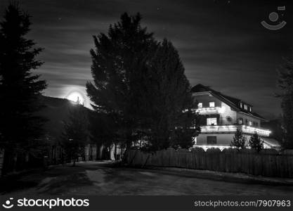 Black and white photo of wooden chalet in wood at starry night