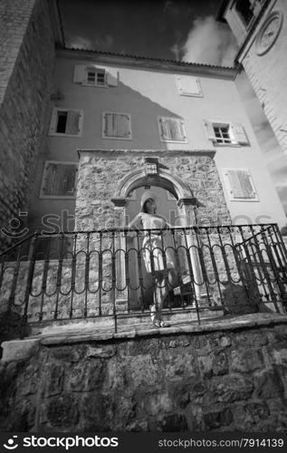 Black and white photo of young elegant woman leaning against railing on ancient street