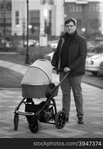 Black and white photo of young happy father walking with baby in pram