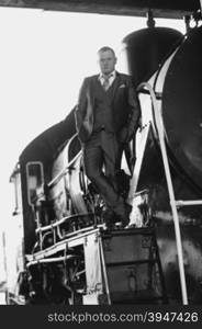 Black and white photo of young man in retro suit standing on old locomotive