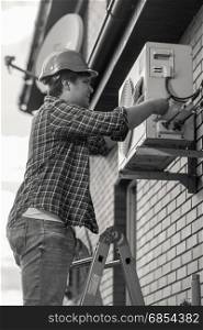 Black and white photo of young man repairing air conditioner