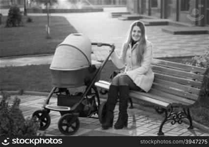 Black and white photo of young mother sitting on bench with baby stroller