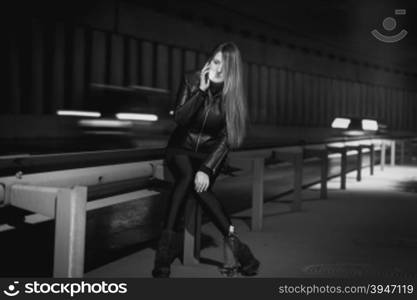 Black and white photo of young stylish woman talking by phone at night highway