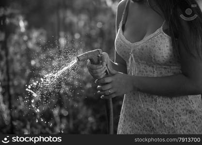 Black and white photo of young woman holding watering hose at garden