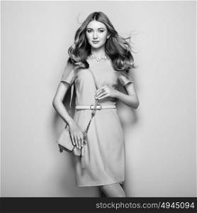 Black and white photo of young woman in elegant dress. Girl posing on a white background. Jewelry and hairstyle. Girl with handbag. Fashion photo
