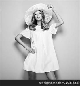 Black and white photo of young woman in elegant dress and summer hat. Girl posing on a white background. Jewelry and clothing. Fashion photo