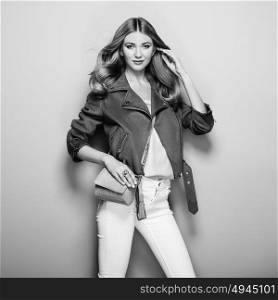 Black and white photo of young woman in leather jacket and white jeans. Girl posing on a white background. Jewelry and hairstyle. Girl with brown handbag. Fashion photo