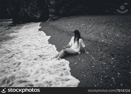 Black and white photo of young woman in white shirt lying on sea beach