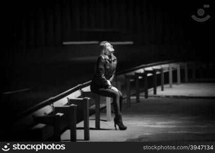 Black and white photo of young woman siting on railings at highway at night