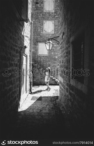 Black and white photo of young woman walking at old narrow street