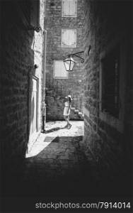 Black and white photo of young woman walking at old narrow street