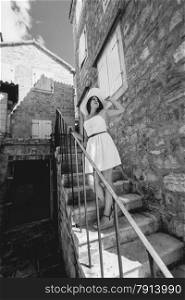 Black and white photo of young woman wearing hat walking down the porch of old building
