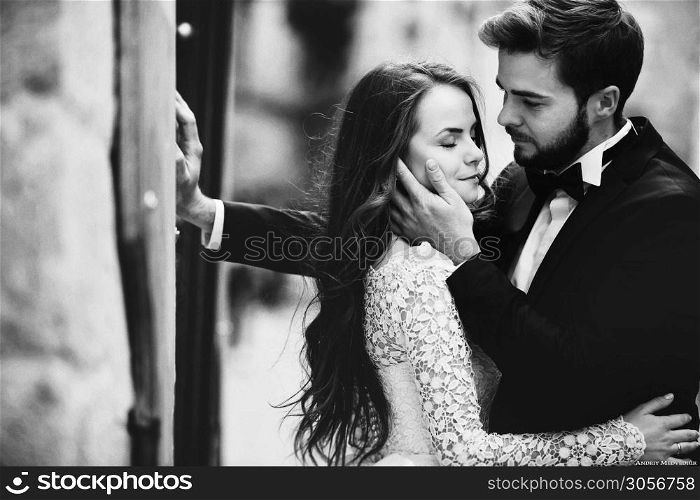 black and white photo. Wedding couple hugging in the old city. stylish bride in white long dress and groom in suit and bow tie. wedding day.. black and white photo. Wedding couple hugging in the old city. stylish bride in white long dress and groom in suit and bow tie. wedding day