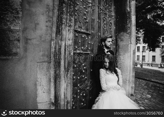 black and white photo. Wedding couple hugs near the vintage green door. Stone walls in ancient town background. bride with long hair in lace dress and groom in suit and bow tie.. black and white photo. Wedding couple hugs near the vintage green door. Stone walls in ancient town background. bride with long hair in lace dress and groom in suit and bow tie