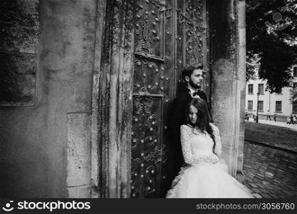 black and white photo. Wedding couple hugs near the vintage green door. Stone walls in ancient town background. bride with long hair in lace dress and groom in suit and bow tie.. black and white photo. Wedding couple hugs near the vintage green door. Stone walls in ancient town background. bride with long hair in lace dress and groom in suit and bow tie
