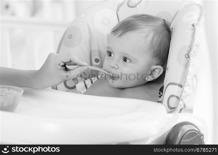 Black and white portrait of adorable baby boy eating porridge from spoon