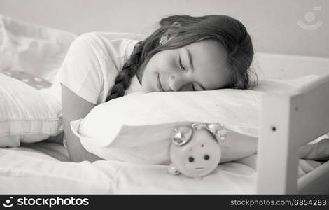 Black and white portrait of beautiful brunette teenage girl sleeping on alarm clock the pillow