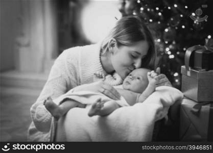 Black and white portrait of beautiful mother kissing baby boy lying in nest at living room