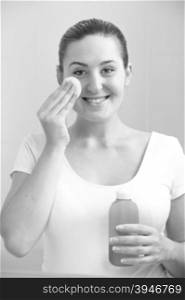 Black and white portrait of beautiful smiling woman cleaning face with lotion
