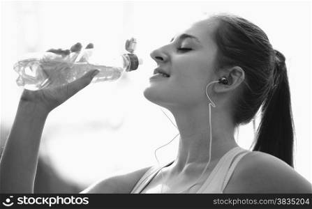Black and white portrait of beautiful sporty woman drinking water while jogging