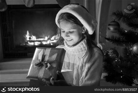 Black and white portrait of cute cheerful girl in Santa hat looking inside of Christmas gift box