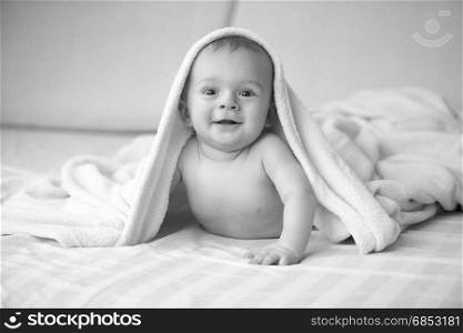 Black and white portrait of cute laughing baby lying under blanket on bed