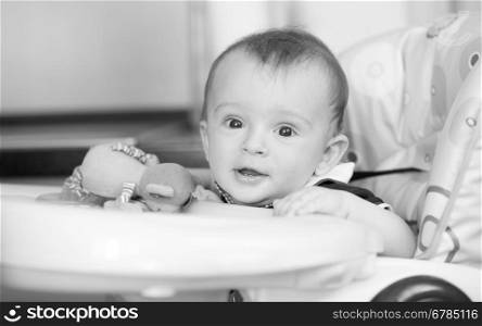 Black and white portrait of cute smiling baby boy sitting in highchair at kitchen