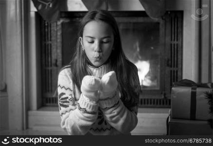 Black and white portrait of cute teenage girl sitting at fireplace and blowing snow from hands